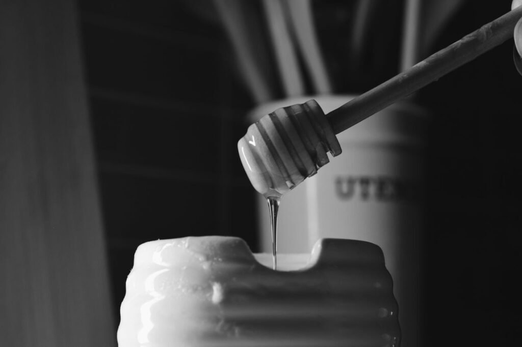 A black and white image of honey dripping from a dipper into a jar, creating a cinematic feel.