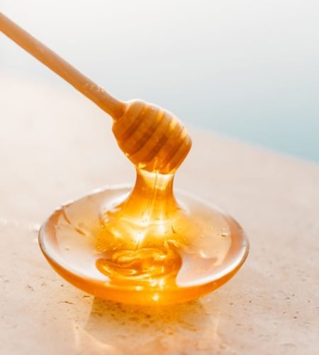 Golden honey flowing from a wooden dipper onto a glass plate, captured in warm daylight.