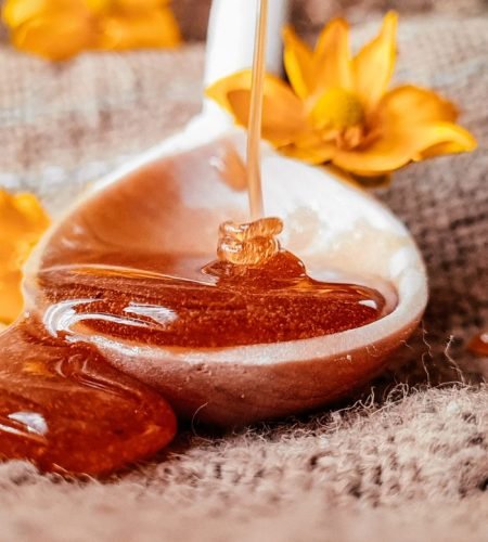 Golden honey dripping from a spoon with yellow flowers for a natural, sweet aesthetic.